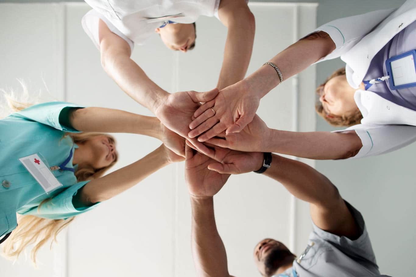 Mitarbeitende einer Arztpraxis legen die Hände zusammen. Ein Symbolbild für Betriebliches Gesundheitsmanagement (BGM): Dabei dreht es sich um die physische, psychische und soziale Gesundheit der Mitarbeitenden.