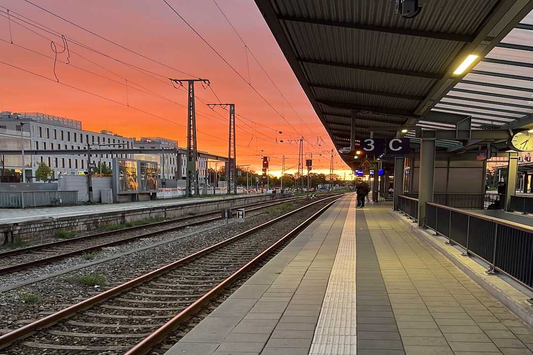 Ein menschenleerer Bahnsteig, der am Horizont im rötlichen Sonnenuntergang endet. 